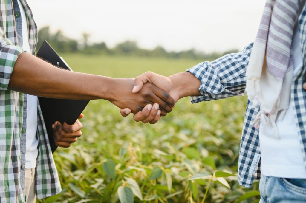 Close-up of African farmers shaking hands on the background of a soybean field.